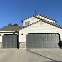 Two-car garage on a white suburban house with gray doors and stone trim under a clear blue sky
