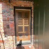Wooden front door set in a brick wall, with a black cat silhouette in the foreground.
