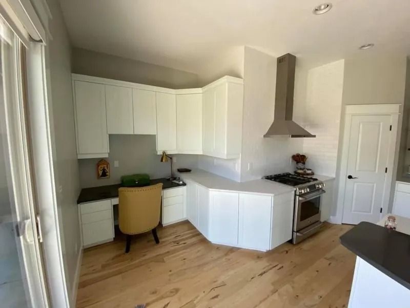 Bright modern kitchen with white cabinets, wood floors, yellow chair, and stainless stove with range hood