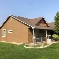 Brown house with a small front porch and green lawn under a clear sky