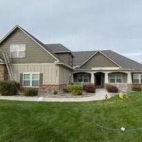 Suburban house with gray siding, stone trim, and a well-kept green lawn under cloudy skies