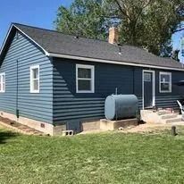 Blue house with white trim, a chimney, and a large propane tank in a grassy yard
