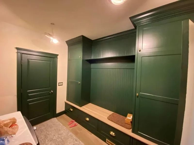 Green built-in bedroom cabinets with drawers, shelves, and a white bed in a room under renovation.