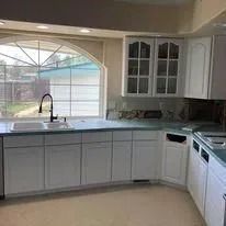 Bright kitchen with gray cabinets, white appliances, a window over the sink, and light countertops.