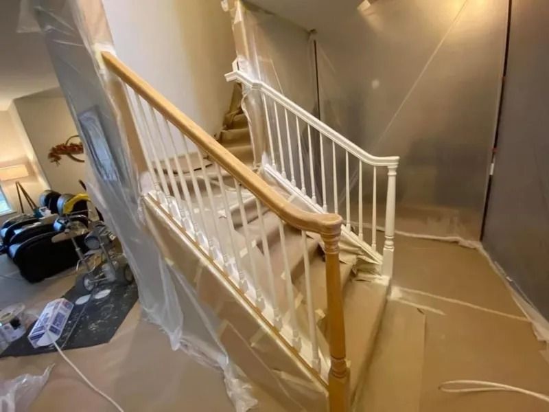 Staircase wrapped in plastic sheeting during home renovation, with white railings and wooden handrail