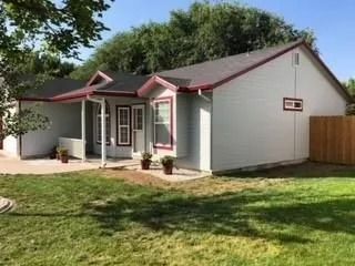 Small white house with red trim, a front porch, and a fenced yard on a sunny day