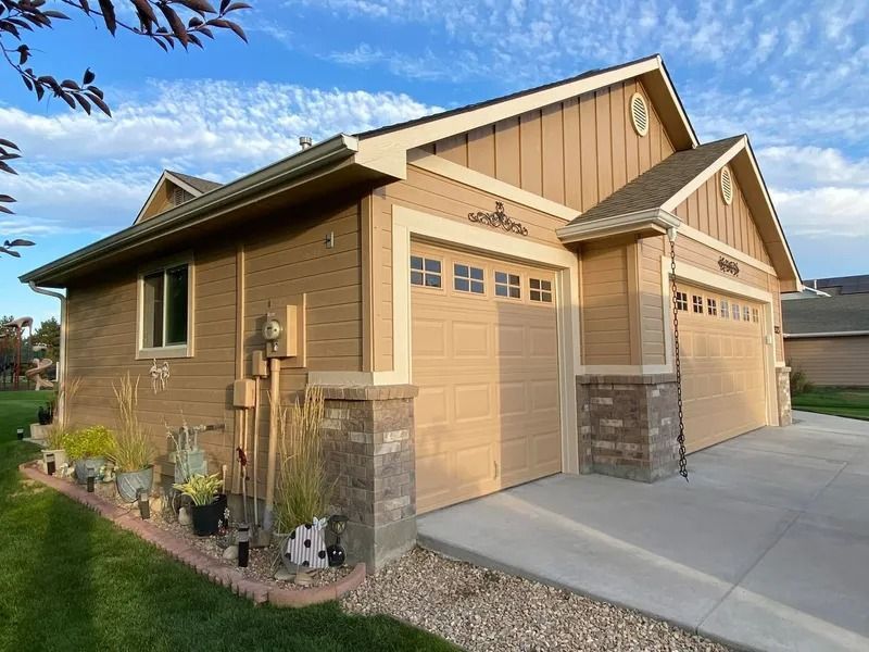 Two-car garage with tan siding, stone accents, and a concrete driveway on a sunny day