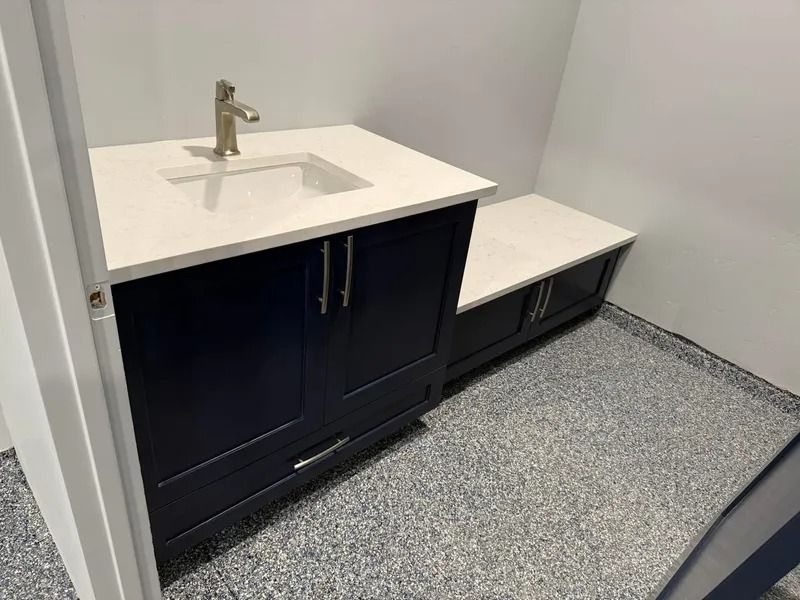 Small bathroom vanity with white sink, dark cabinets, and a built-in bench on a speckled floor.