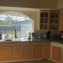 Kitchen sink under large arched window with sunlight and wooden cabinets