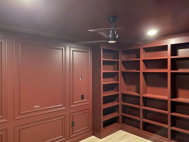 Built-in red wood shelves and cabinets in a carpeted room with ceiling fan and recessed lights