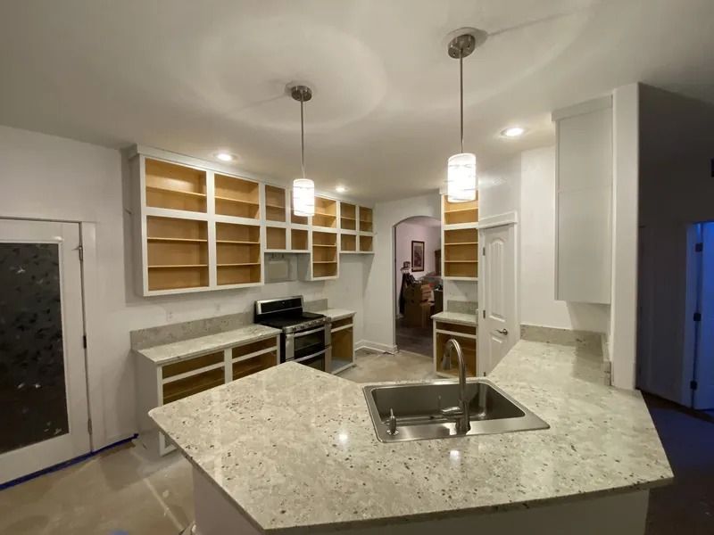 Modern kitchen with granite island, pendant lights, and open wooden shelves under renovation