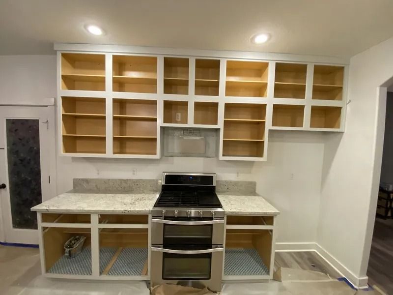 Empty kitchen with white cabinets, open shelves, and a stainless steel stove centered on a light stone backsplash.