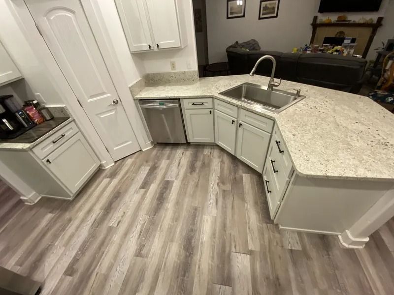 Modern kitchen with light cabinets, white countertops, curved island, and gray wood flooring