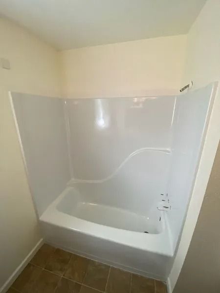 Small bathroom with white tub, clear shower surround, and brown tile floor