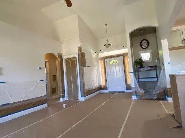 Empty living room with taped-off floor and white walls, view toward front door and fireplace.