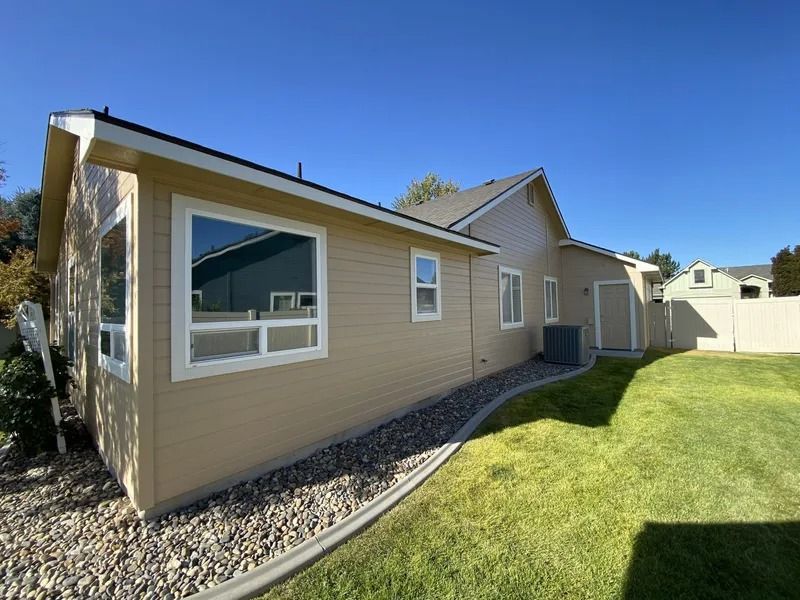 Single-story beige house with a large window, gravel border, and green lawn under a blue sky