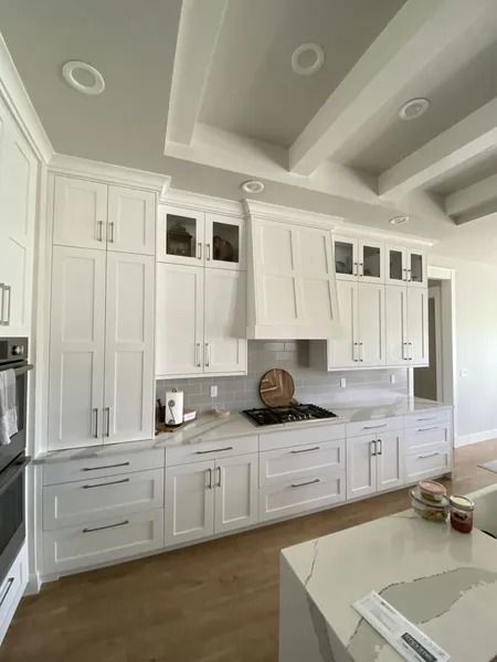 Bright white kitchen with tall cabinets, wood floor, and coffered ceiling.