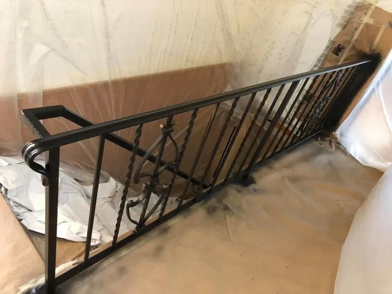 Black metal stair railing leaning against a wall in a room with plastic-covered surfaces.