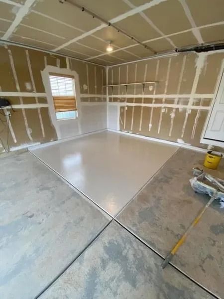 Unfinished garage interior with drywall, taped seams, and a freshly coated white floor center.