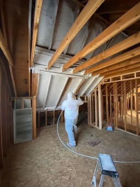 Person spray-insulating exposed attic rafters in an unfinished house.