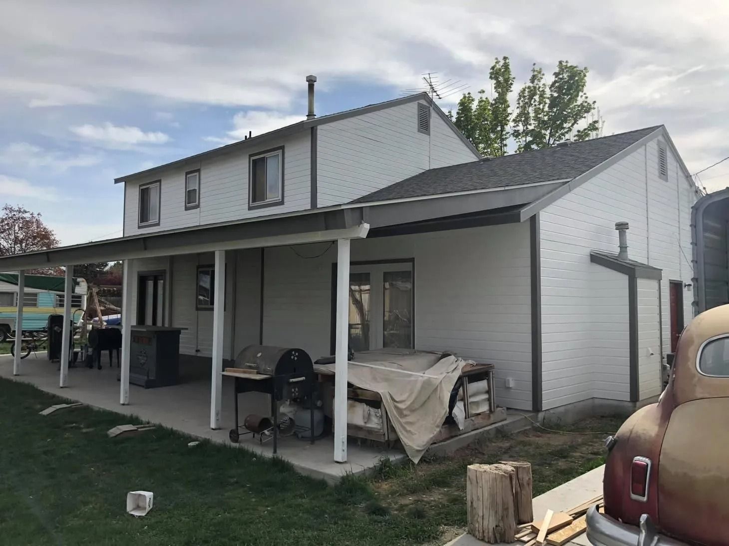 Two-story gray house with a covered porch, yard, and parked car at the right edge
