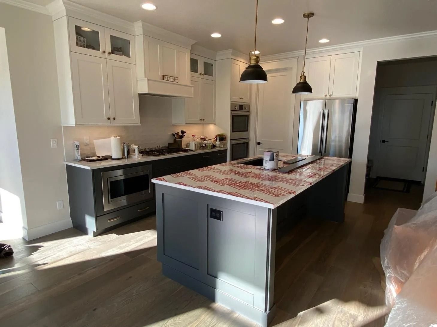 Modern kitchen with white cabinets, gray island, black pendant lights, and stainless steel fridge