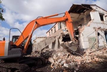 Orange excavator demolishing a damaged building amid rubble and debris