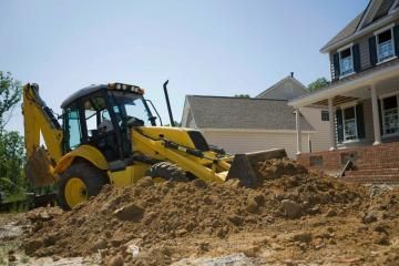 Yellow backhoe loader moving dirt at a house construction site