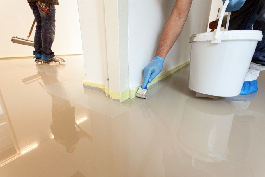 Workers applying glossy floor coating in a room with a white bucket and paint roller