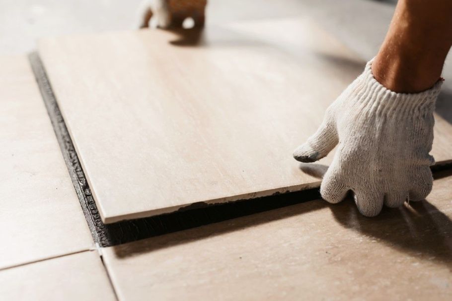 Gloved hands fitting a light wood floor plank into place during installation