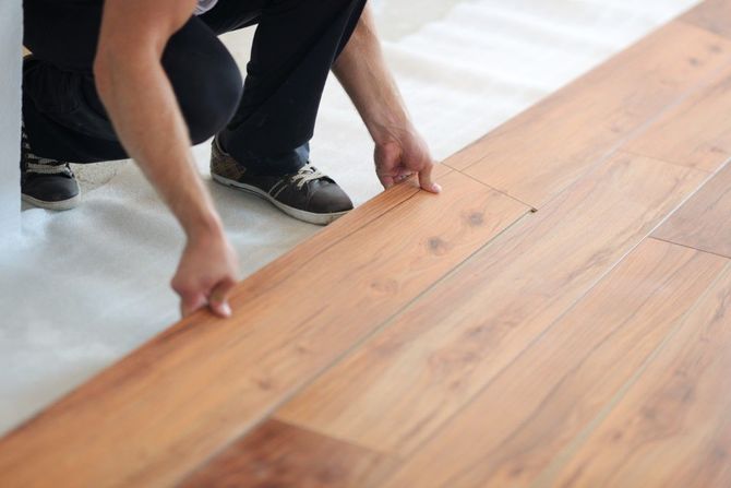Two people aligning wood flooring planks on a bright floor.