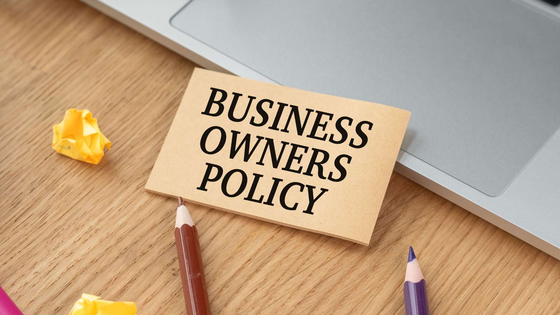 Business Owners Policy card on a wooden desk with pencils and a laptop corner