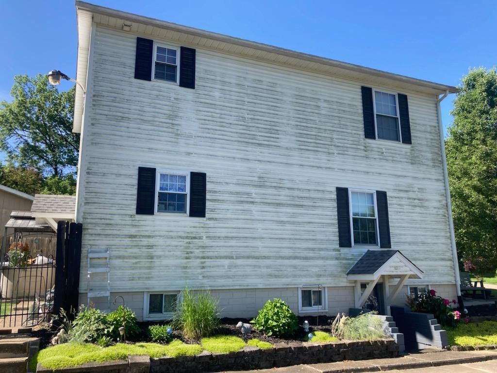 A white house with black shutters is sitting on top of a lush green hillside. | Louisville, Ohio | Mongiardo Power Wash