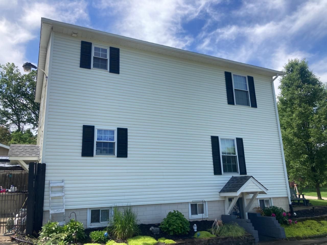 A white house with black shutters and a blue sky in the background. | Louisville, Ohio | Mongiardo Power Wash