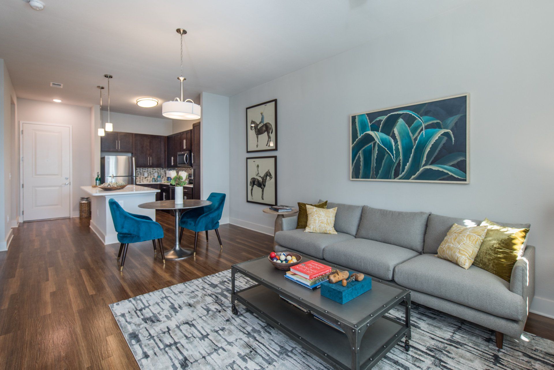 Modern living room with a gray sofa, blue accent chairs, a wooden dining table, and kitchen area with dark cabinetry at Silver Collection at Carl D. Silver Parkway in Fredericksburg, VA.