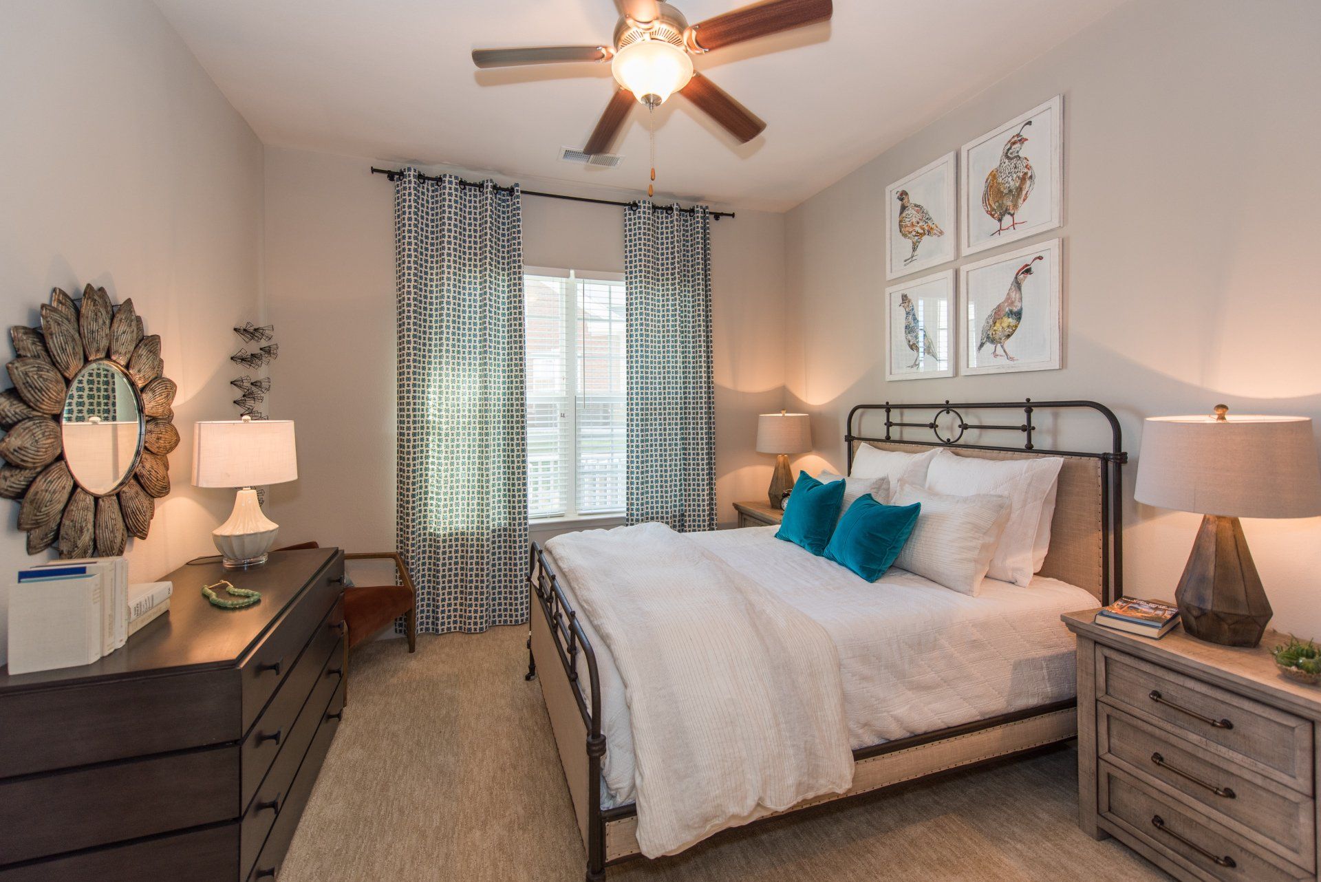 A bedroom with a queen bed, dark wood dresser, nightstand, mirror, and four bird-themed framed prints on the wall at Silver Collection at Carl D. Silver Parkway in Fredericksburg, VA.