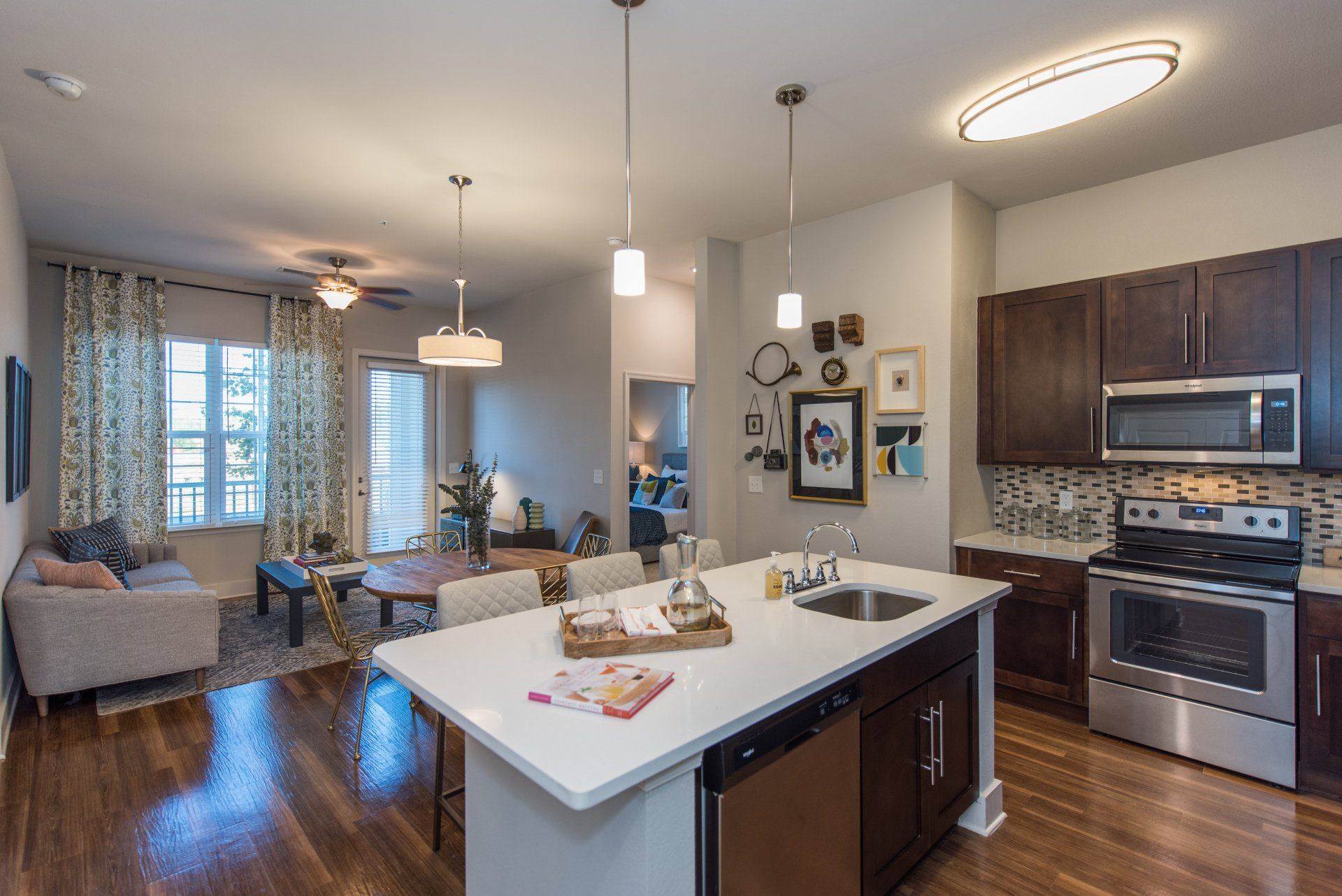 An open-concept apartment with a kitchen island, dark wood cabinets, stainless appliances, and a living area with a sofa at Silver Collection at Carl D. Silver Parkway in Fredericksburg, VA.