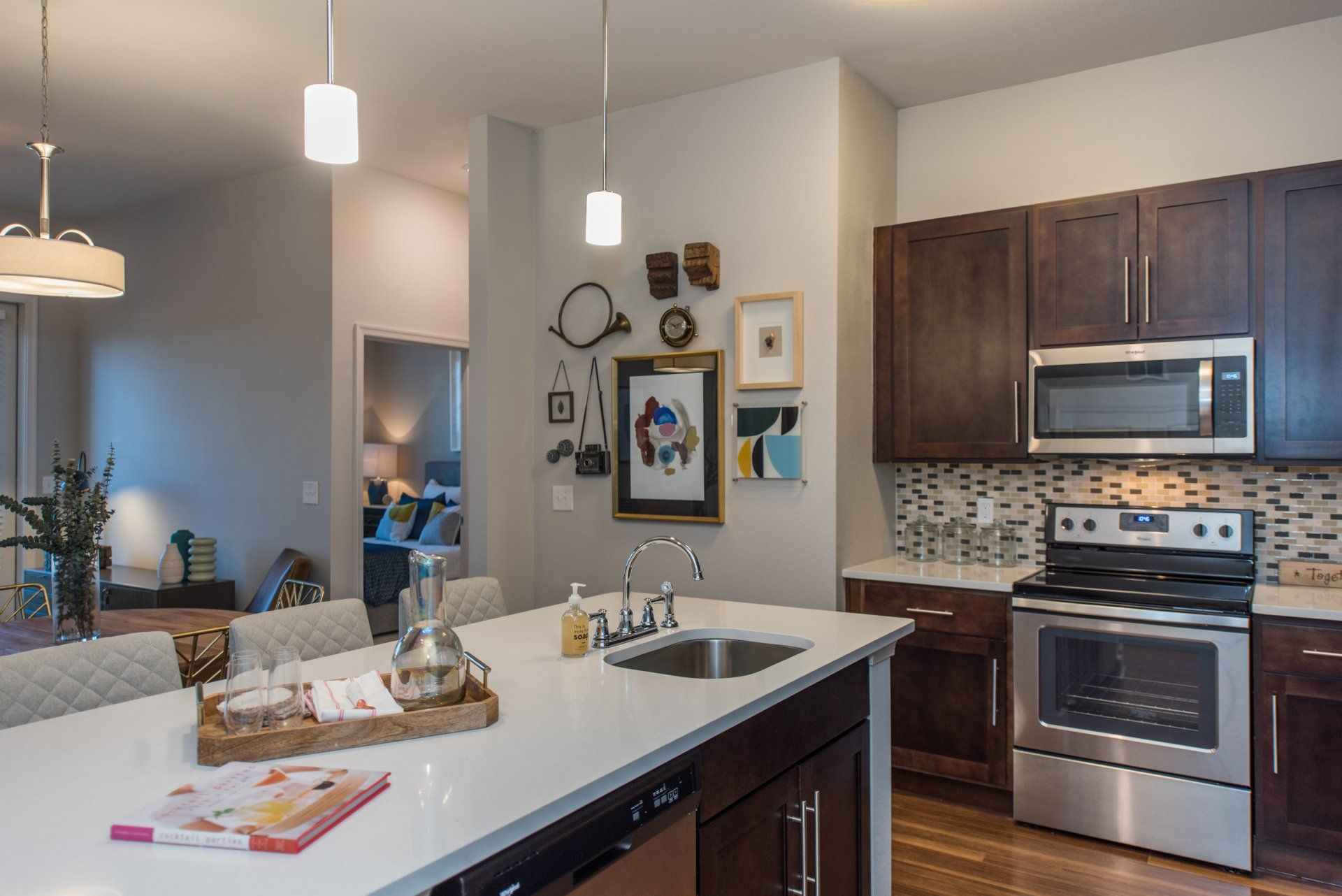 A modern kitchen with dark wood cabinets, stainless steel appliances, a white island countertop, and a decorative wall at Silver Collection at Carl D. Silver Parkway in Fredericksburg, VA.