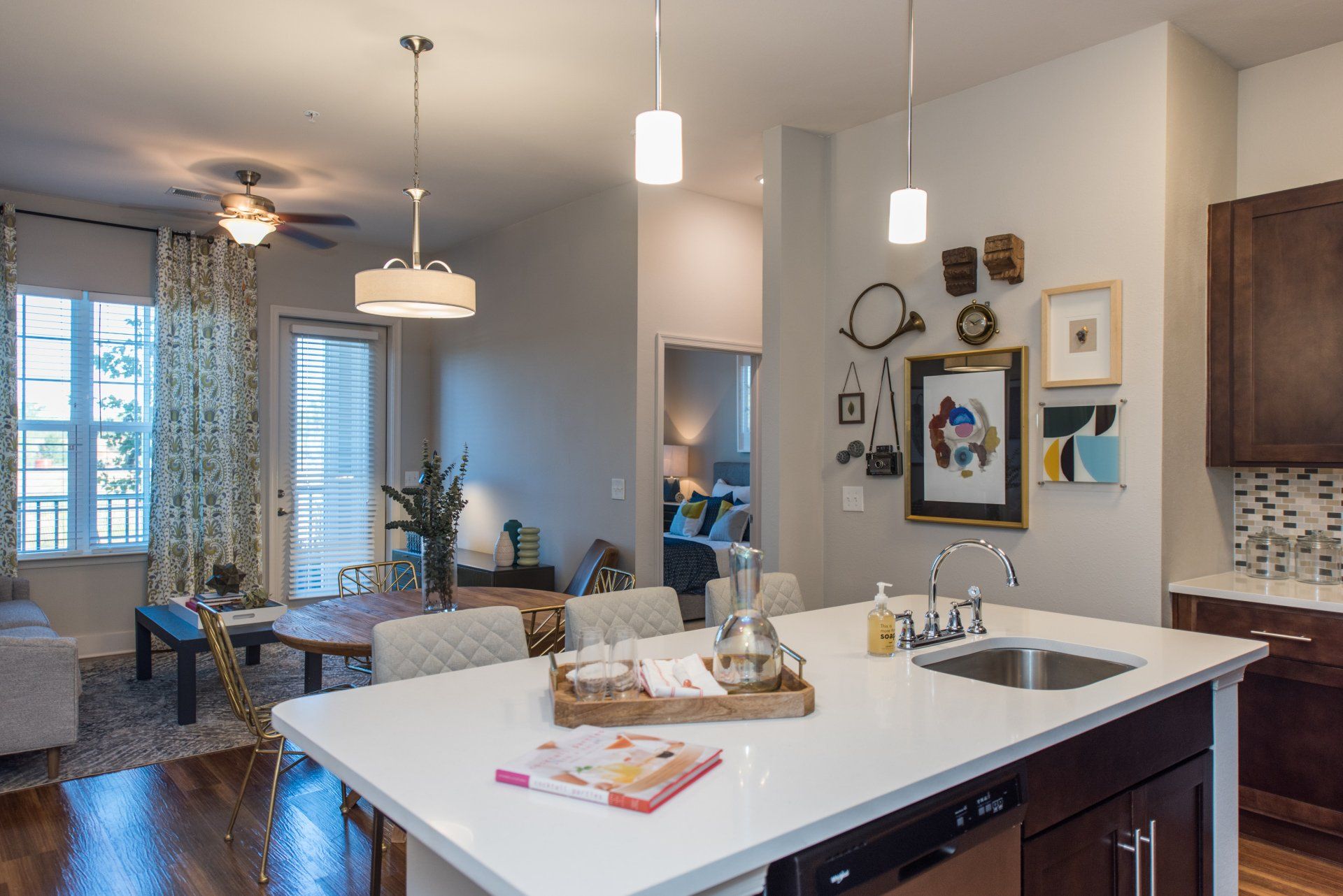 A kitchen island with a white countertop and sink in the foreground, overlooking an open-plan dining and living area at Silver Collection at Carl D. Silver Parkway in Fredericksburg, VA.