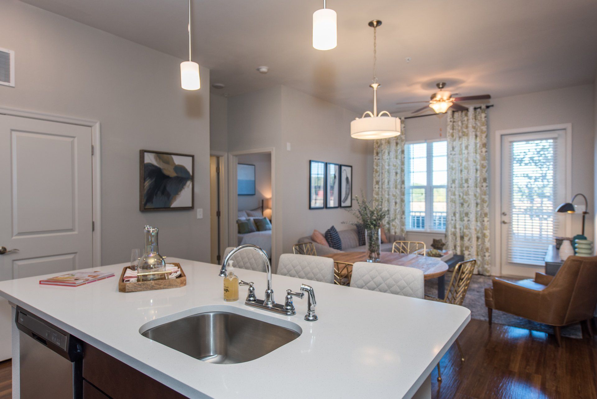 A bright, modern kitchen island with a sink in the foreground, overlooking an open-plan dining and living room area at Silver Collection at Carl D. Silver Parkway in Fredericksburg, VA.