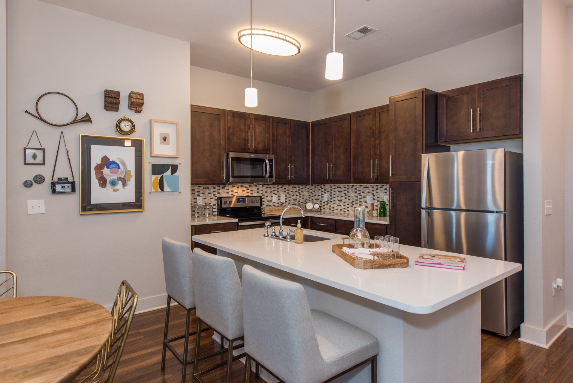 A modern kitchen with brown cabinets, stainless steel appliances, a white island with three stools, and wall art at Silver Collection at Carl D. Silver Parkway in Fredericksburg, VA.