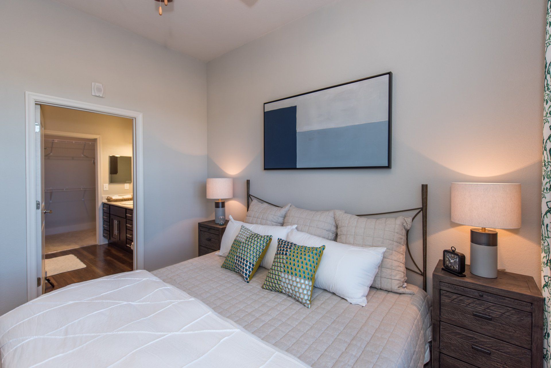 A bedroom with a queen bed featuring a quilted white comforter, neutral pillows, bedside lamps, and framed wall art at Silver Collection at Carl D. Silver Parkway in Fredericksburg, VA.