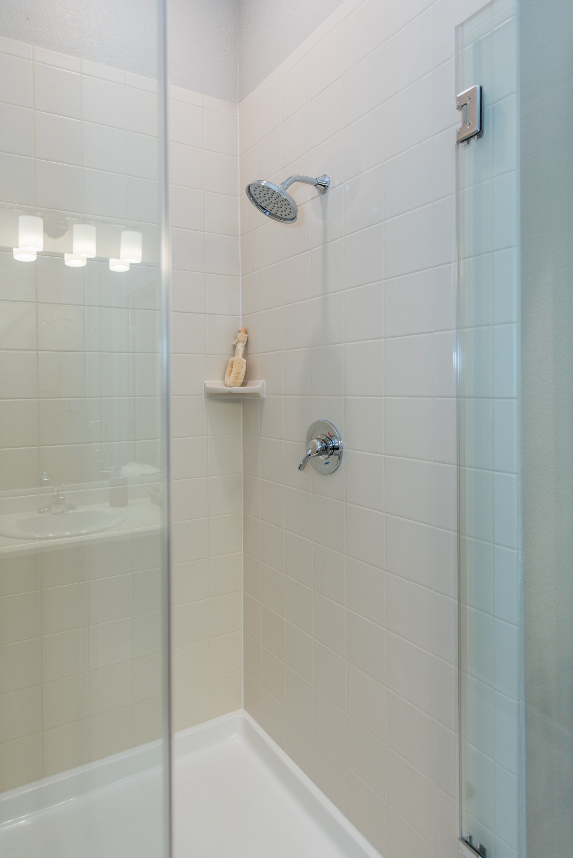 A white-tiled shower stall with a glass door, wall-mounted showerhead, and a small built-in corner shelf at Silver Collection at Carl D. Silver Parkway in Fredericksburg, VA.