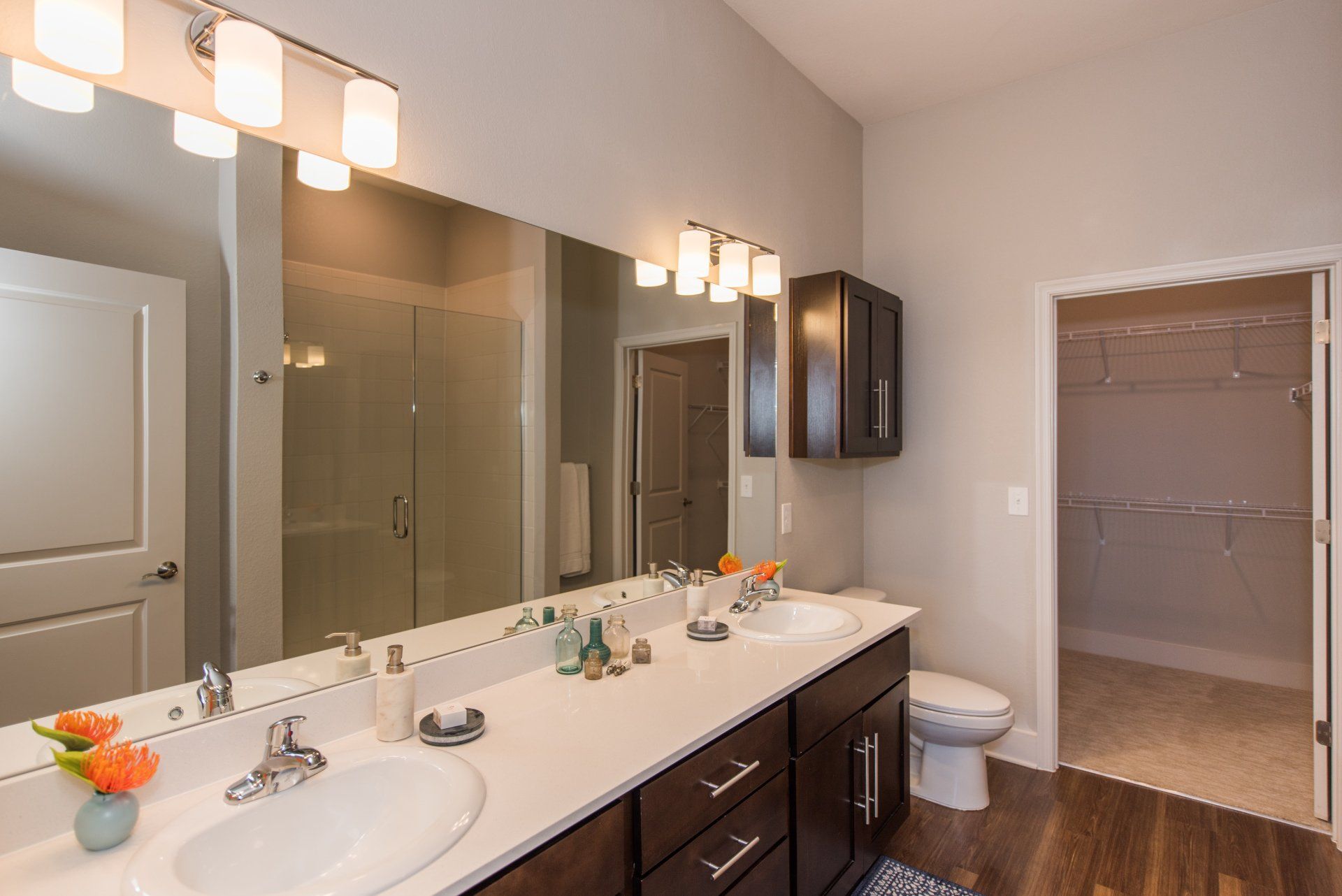 A modern bathroom with a double vanity, large mirror, shower, and walk-in closet against neutral-colored walls at Silver Collection at Carl D. Silver Parkway in Fredericksburg, VA..
