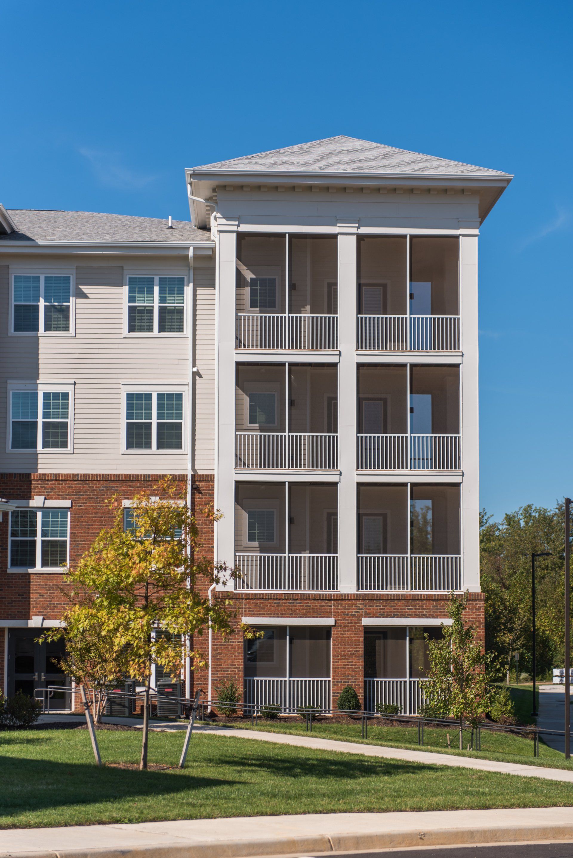 A modern four-story apartment building with brick and beige siding, featuring stacked screened-in balconies at Silver Collection at Carl D. Silver Parkway in Fredericksburg, VA..