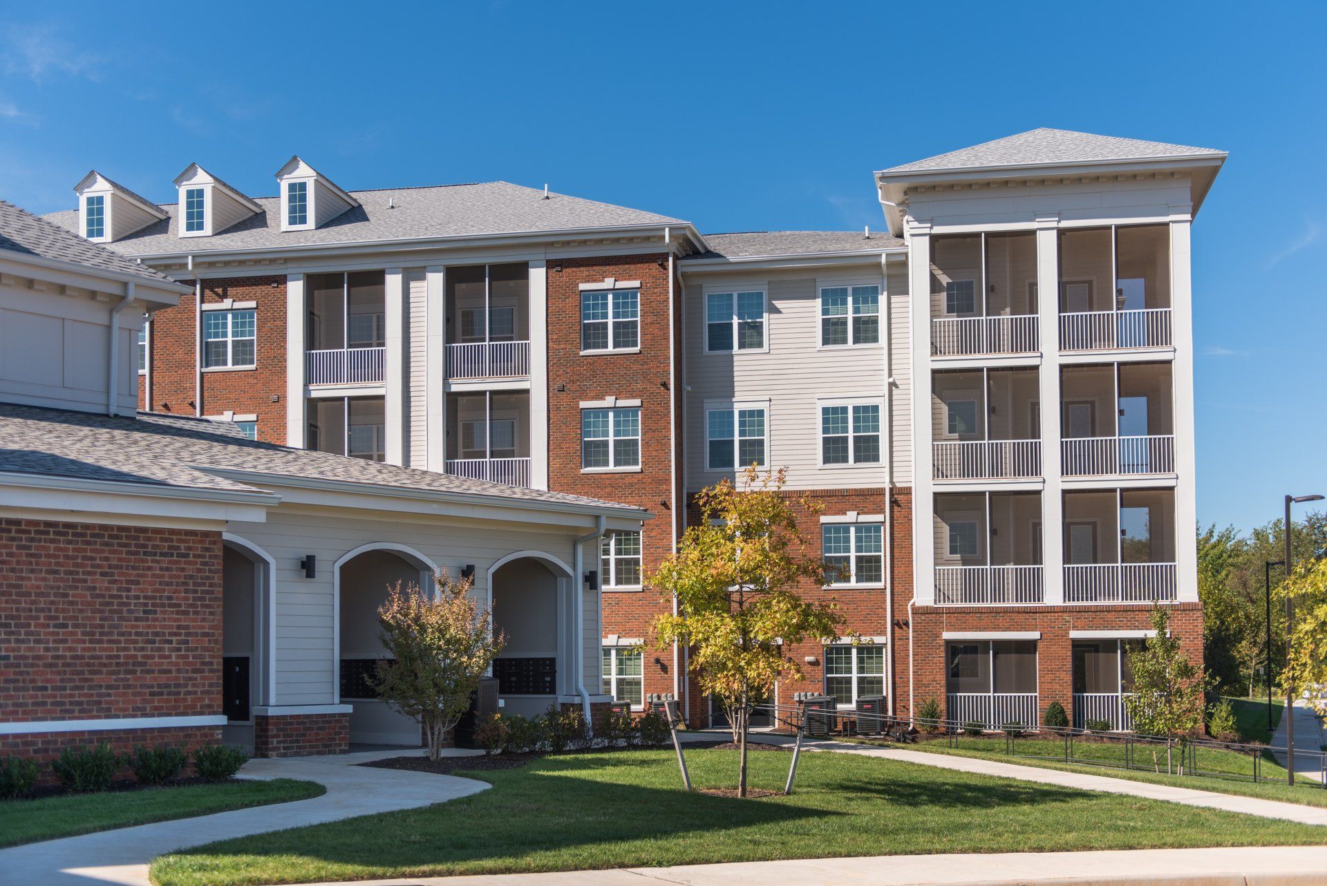 A four-story brick and stucco apartment building with screened balconies and a landscaped lawn on a sunny day at Silver Collection at Carl D. Silver Parkway in Fredericksburg, VA..