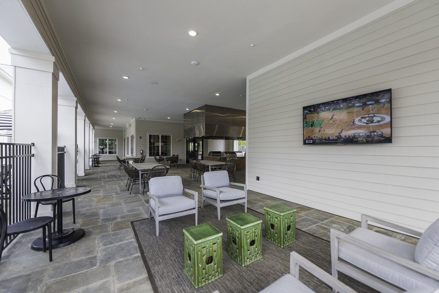 An outdoor patio area with a television on the wall, lounge chairs, small green tables, and bistro-style seating at Silver Collection at Carl D. Silver Parkway in Fredericksburg, VA..