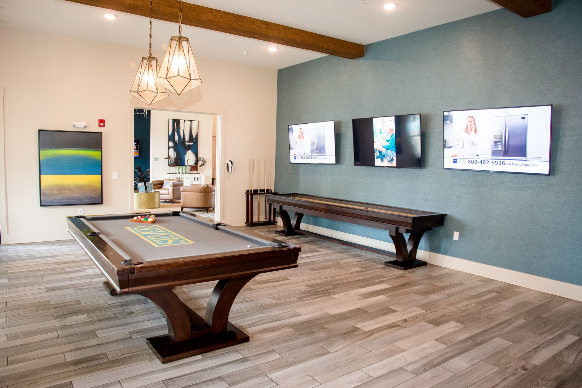 A game room with a pool table, shuffleboard table, and three televisions mounted on a blue wall.