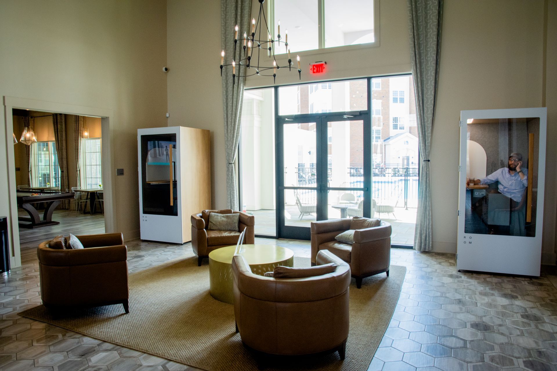 A spacious lounge area with armchairs and a phone booth. A person is inside the booth on the phone.