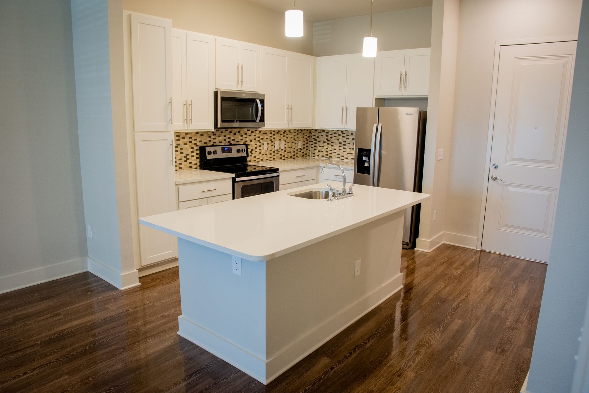 Modern kitchen with white cabinets, stainless steel appliances, a white island, and dark wood floors.